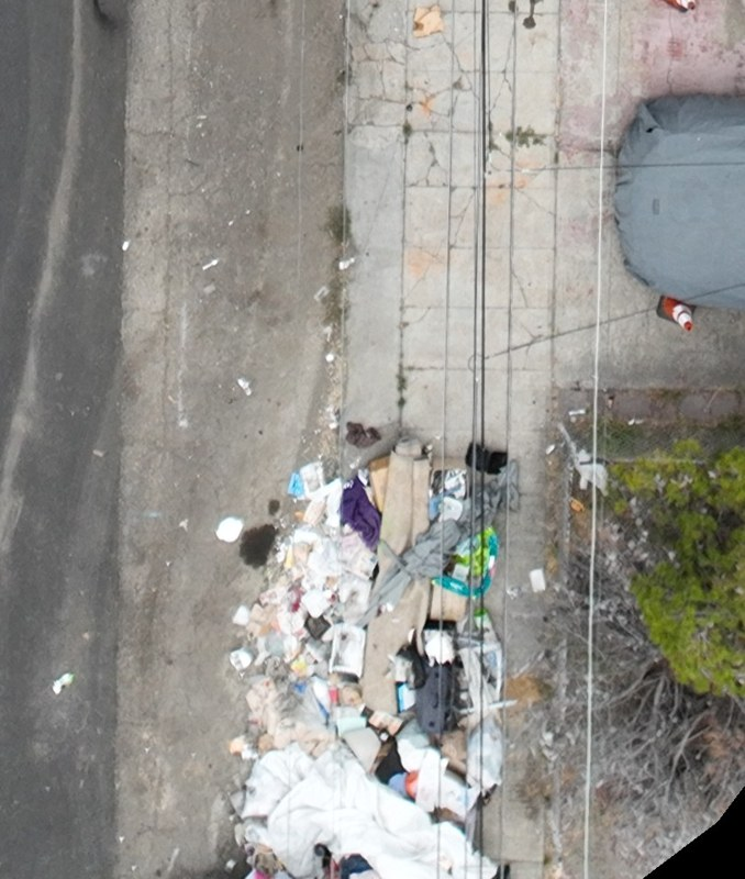 A long pile of discarded materials along a sidewalk beneath overhead wires