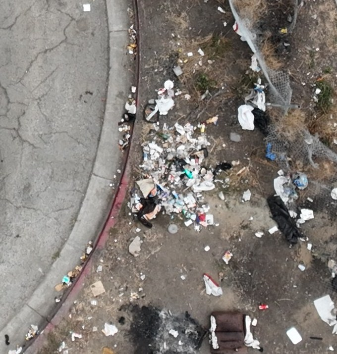 Loose waste spread along a curved curb beside a chain-link fence