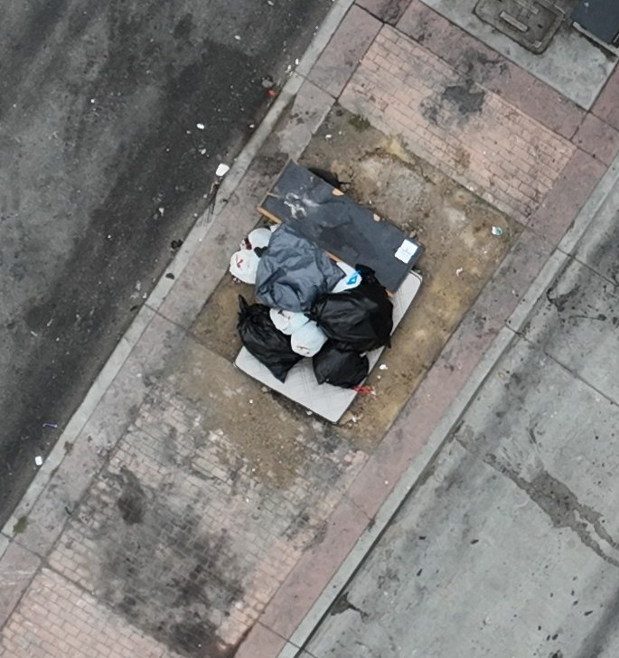 Bagged waste and bulky discarded material on a paved traffic island