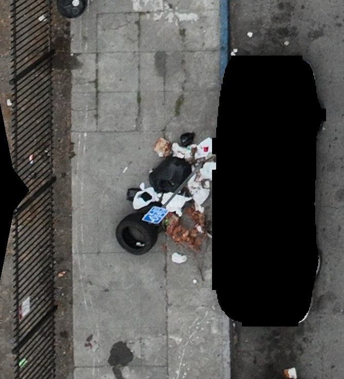 A discarded tire and mixed waste beside a redacted vehicle
