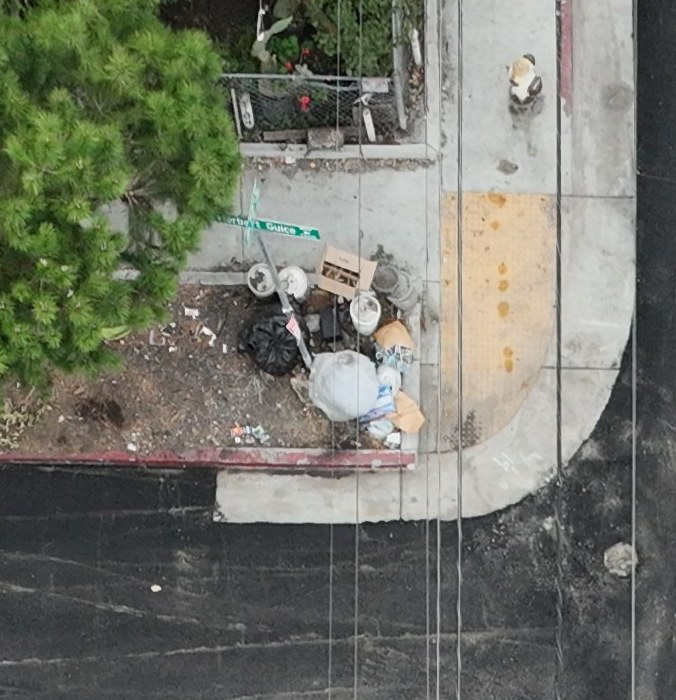 Bagged and loose waste at a street corner beside a fence